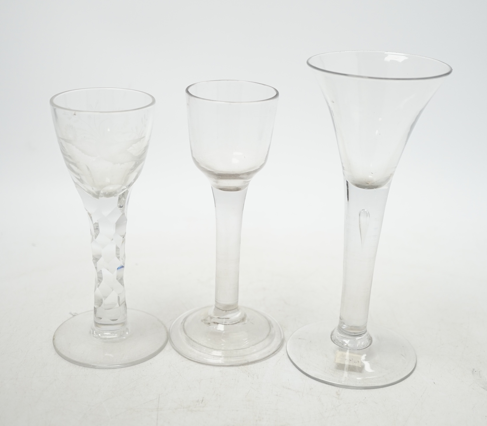 Three 18th century wine glasses; a drawn trumpet glass, another with a bell shaped bowl and folded foot and an engraved glass with a faceted stem, tallest 16.5cm. Condition - good